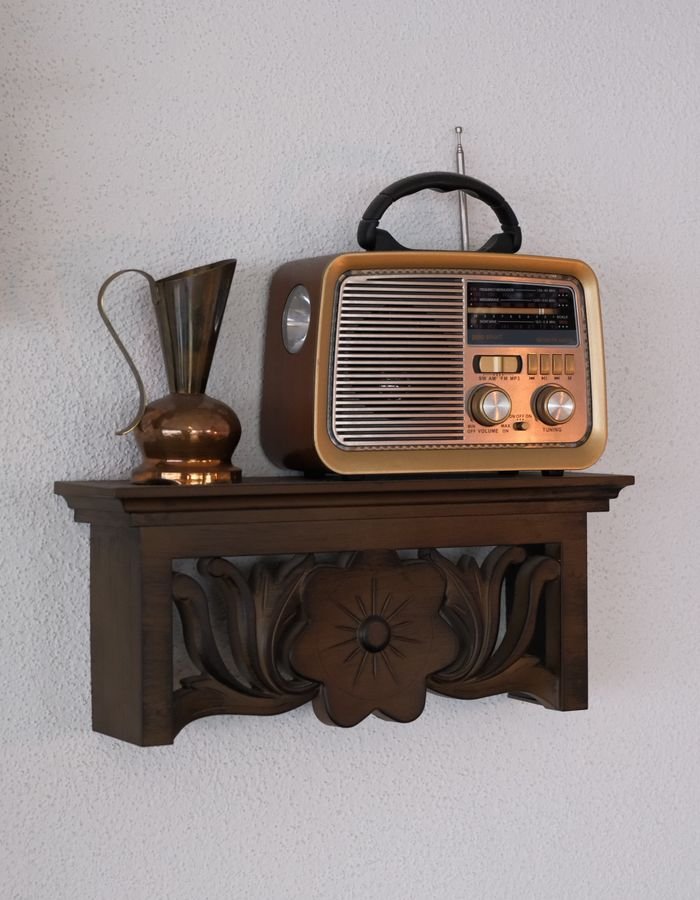 A retro radio and copper vase displayed on a carved wooden wall shelf