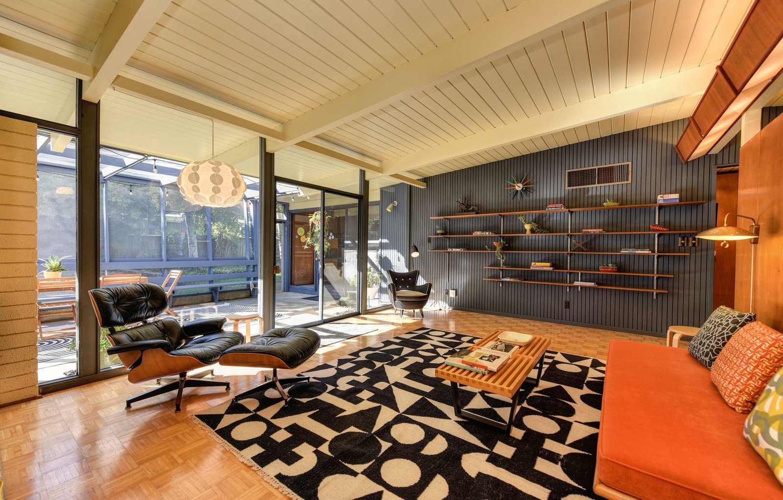 A styled mid-century modern living room with a leather lounge chair, walnut shelving and a globe pendant light