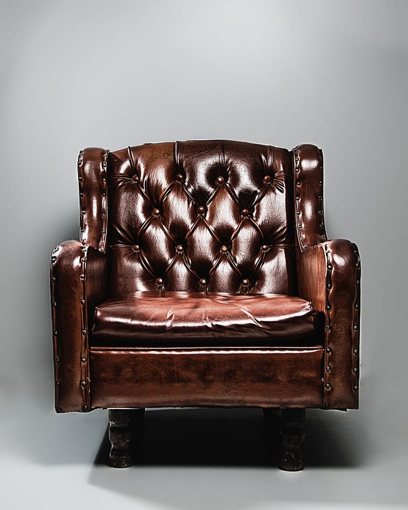 A deep-buttoned brown leather club chair photographed against a plain studio backdrop